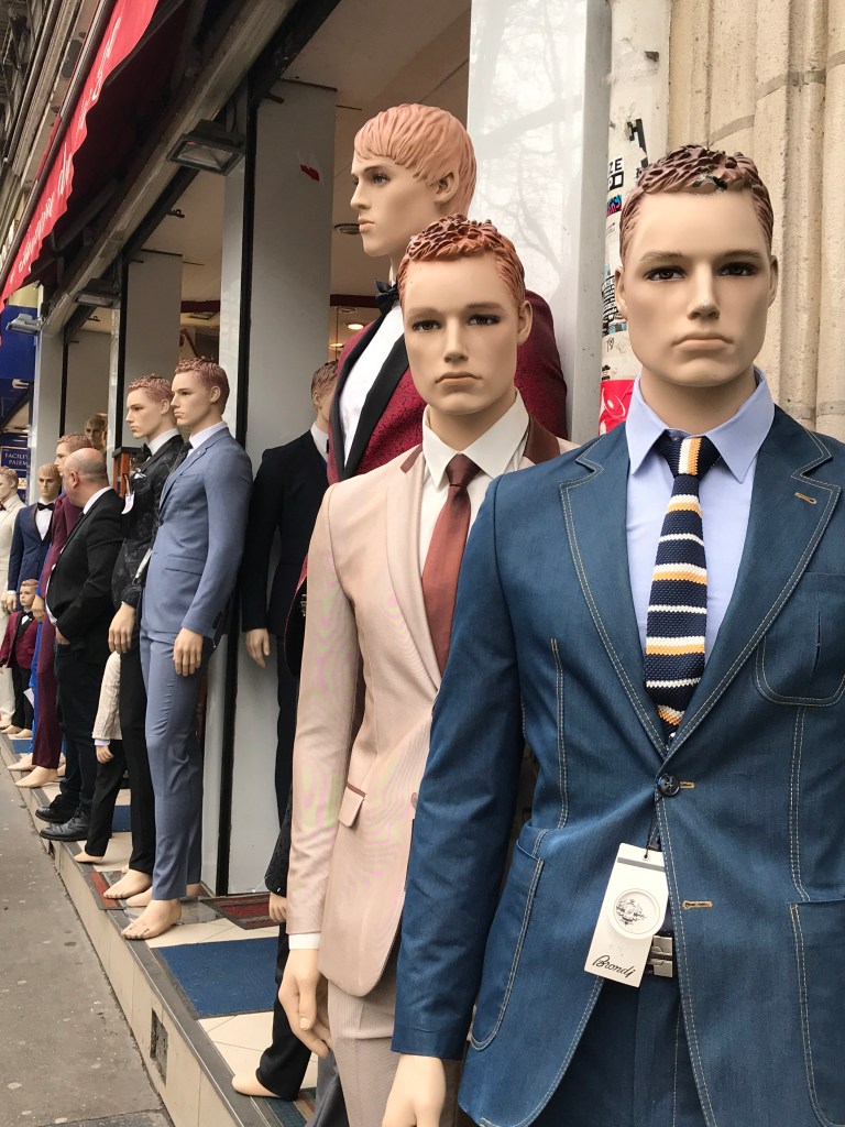 Mannequins in a row down te street with a real person in the middle of them.